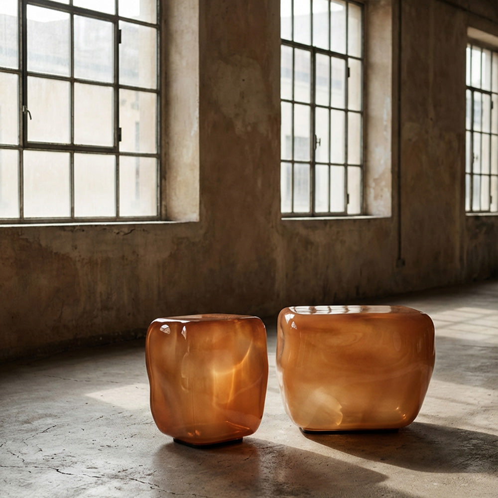 Two modern, Ishi Glass tables in a golden caramel colour, placed on a concrete floor in a rustic industrial loft with large windows.